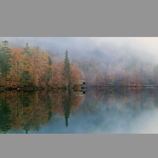 Misty autumn lake surrounded by colorful fall trees and a small cabin